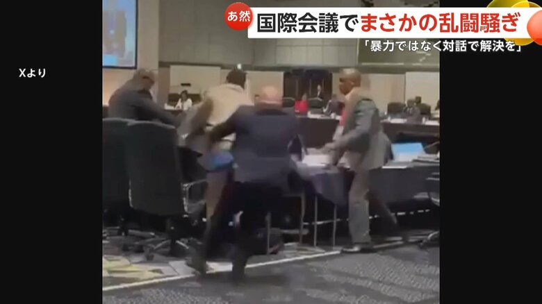 ベージュのスーツの男性に背中から飛び掛かる紺色のスーツの男性