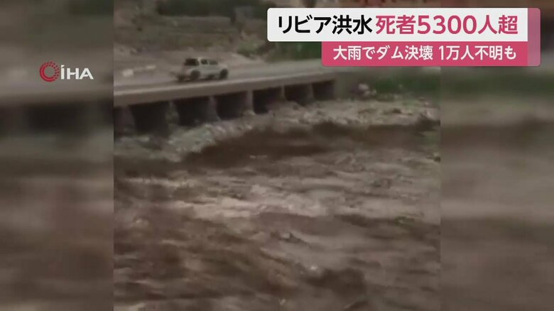 橋の上を通り過ぎる車。川は濁流になり押し寄せている