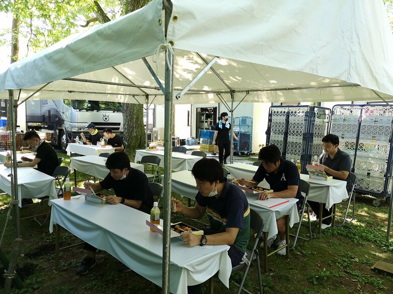 一方向に間隔を空けて座り、黙って食事をする様子