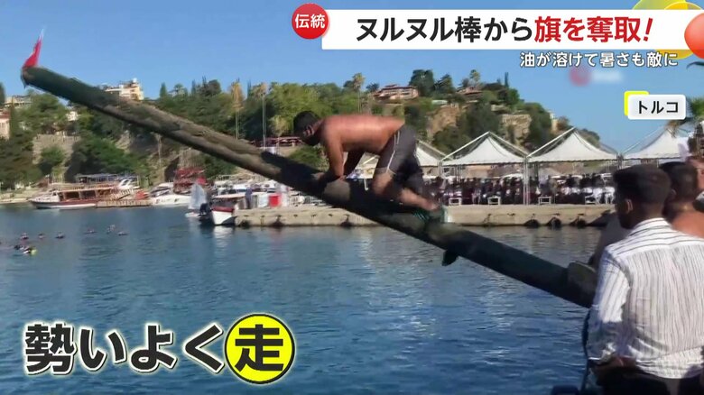 長い棒の先に立てられた国旗を取ろうと勢いよく走る男たち