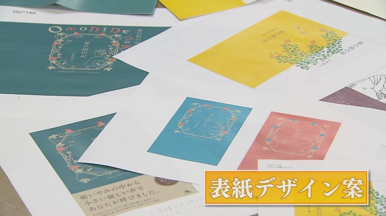 机の上に広げられた「思ひ出の記」の表紙デザイン案　青・緑・黄色など色とりどりの案が比較・検討された跡をとどめている
