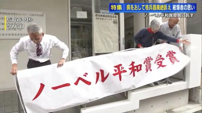 ノーベル平和賞受賞の横断幕を掲げる箕牧さん（右）