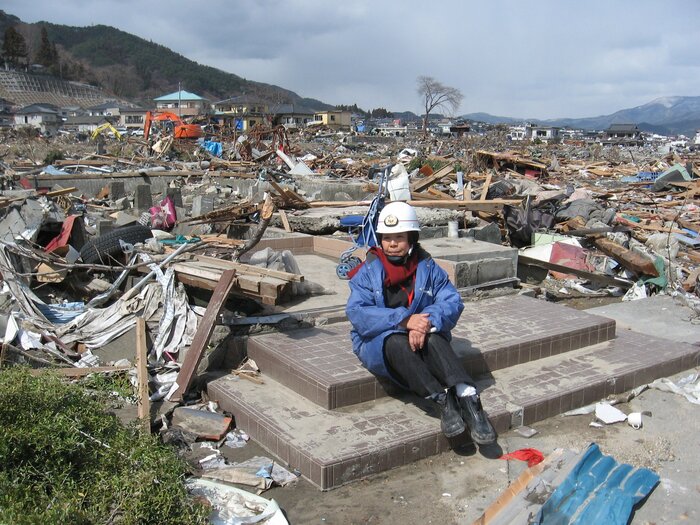 流された実家の玄関前に座り込む鵜浦さん (©LOVETONIPPONPROJECT)