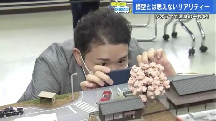 ジオラマの駅と鉄道模型を撮影する野川アナ