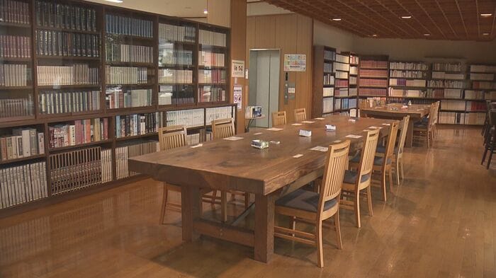 安来市立図書館　長い木製テーブルと椅子が整然と並び、壁面には本がびっしりと収められている