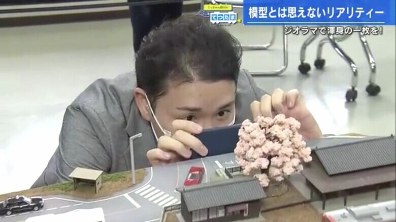 ジオラマの駅と鉄道模型を撮影する野川アナ