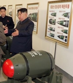 北朝鮮が発表した「火山31」型核弾頭?後ろに搭載する兵器のイラストポスターが見える。(労働新聞・3月28日)