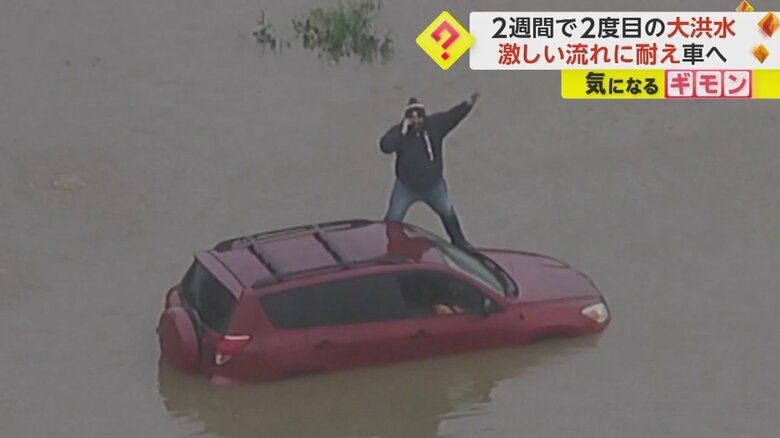 水に囲まれた車の上で手を振る男性