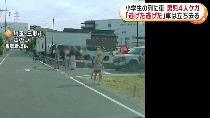 車の周りに、多くの児童の姿が確認できる。車のそばには、黒い服を着た男が(埼玉・三郷市 14日)