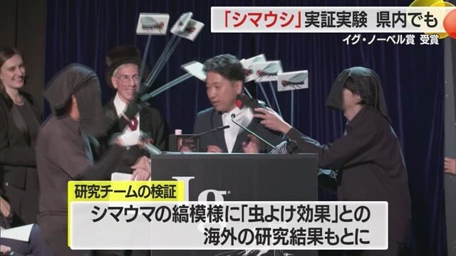 スピーチの最中、共同研究者たちが虫の絵をつけた棒を振って、虫がたかる演出をしていた