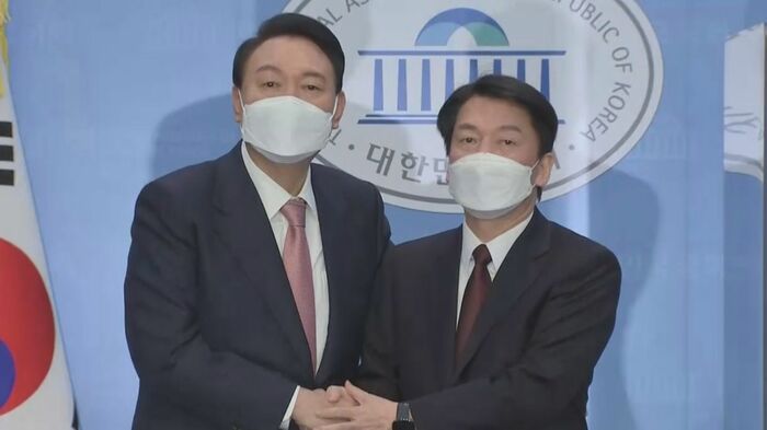会見を終え手を取り合う、尹氏(左)と安氏(右) 安氏は尹氏の支援に回る