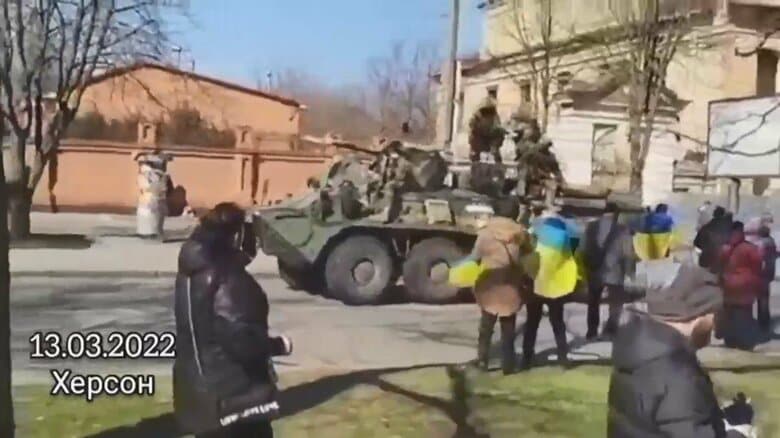 ウクライナ南部・へルソン　13日、市民が抗議するそばをロシア軍とみられる軍用車両が走行