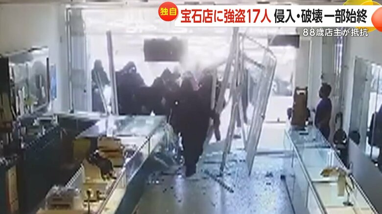 店の前に止まった3台の車から降りてきたフードなどをかぶった集団