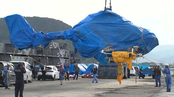 海から引き揚げられブルーシートに覆われたヘリの機体(2025年4月10日)