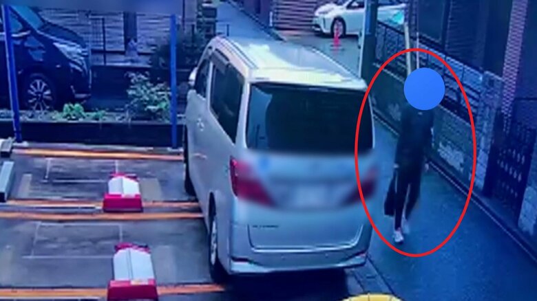駐車場に止めてある車に目をやる人物