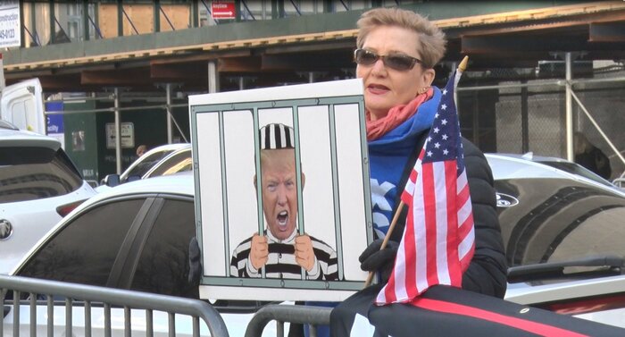 トランプ反対派の女性は収監される様子を模したプラカードでアピール