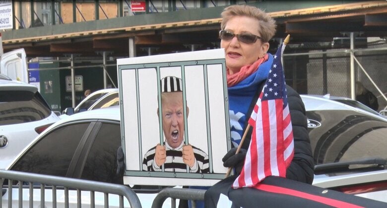 トランプ反対派の女性は収監される様子を模したプラカードでアピール