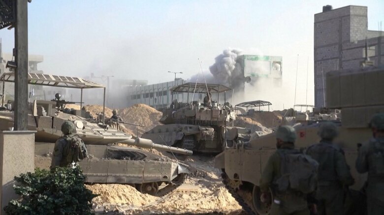 ガザに展開するイスラエル軍車両 砲塔の上に屋根のような装甲を付けたメルカバMk.4M戦車（左と画面中央）ナメル重装甲兵員輸送車（右端）（11月4日）