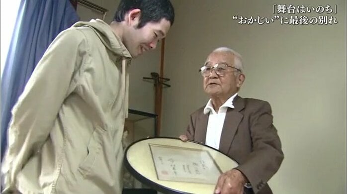 今村昌平監督の色紙を菅原さんに見せる岡田さん