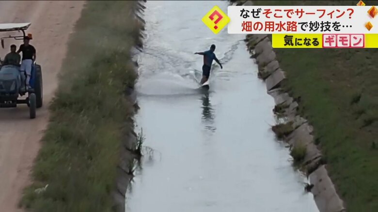 トラクターに引っ張られ用水路でサーフィンをする男性