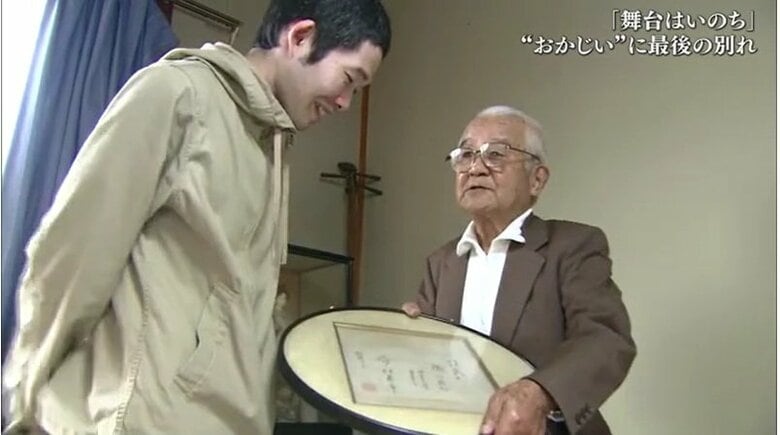 今村昌平監督の色紙を菅原さんに見せる岡田さん
