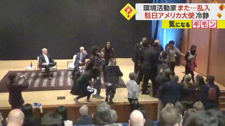 スーツを着た男性が活動家に舞台から降りるよう促す様子
