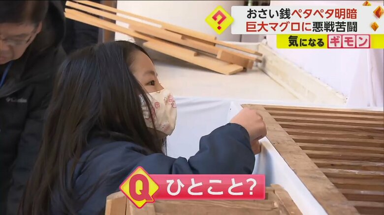 招福マグロにさい銭を貼り付けようとしている子供