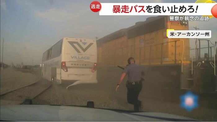 レールと貨物列車に阻まれるバスを追う警察官