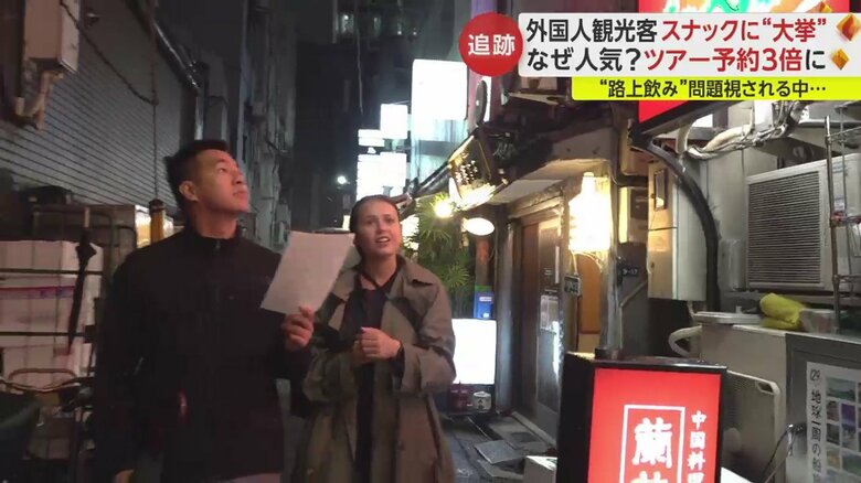 スナックに入る前、漢字の店名が書かれた紙を手に店を探す2人