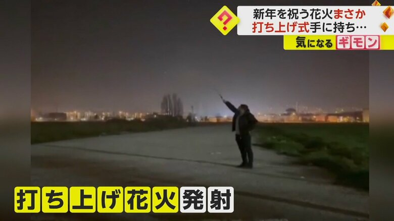 打ち上げ花火を手に持ち、夜空に向ける男性