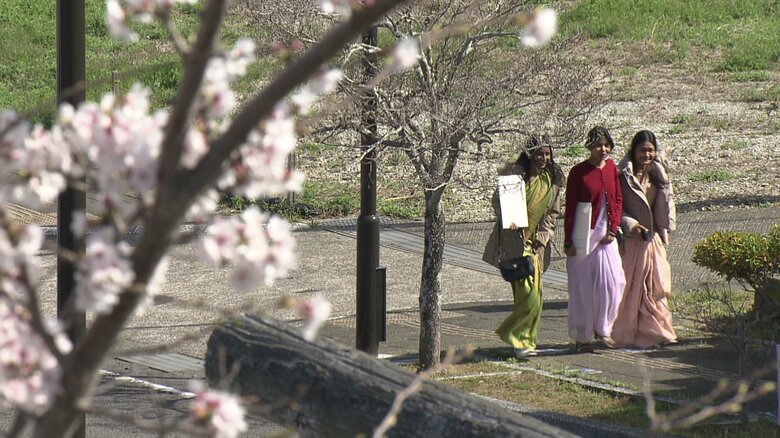 満開の桜の中、民族衣装で留学生が入学式に臨んだ