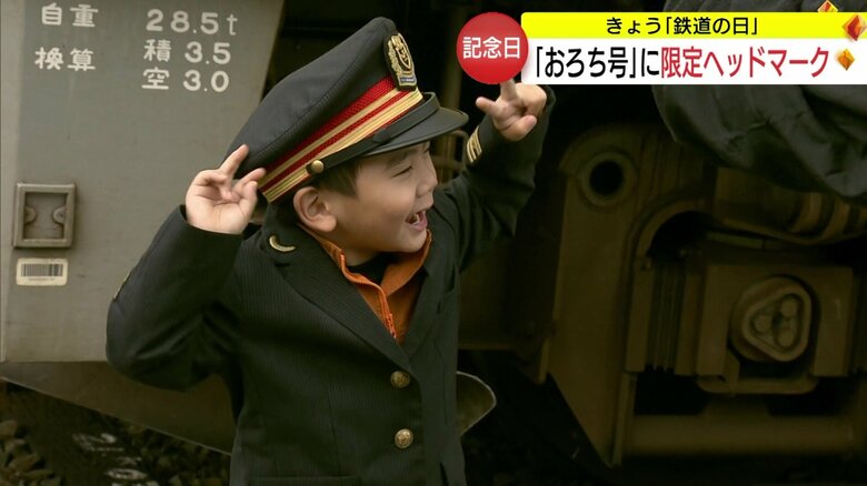 駅員の制服を身にまとい、列車と記念撮影する子ども