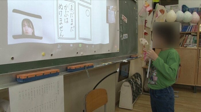 かるた作りの授業でカメラの前に立って作品を見せる小学生(2023年1月)