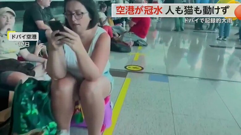 飛行機の運航が再開しても、疲れ切った様子で床に座り込む人の姿