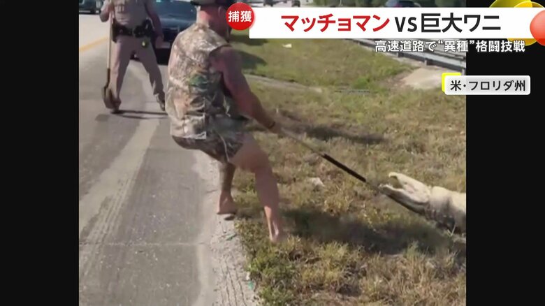 棒で首根っこを押さえ、距離を取るマッチョマン