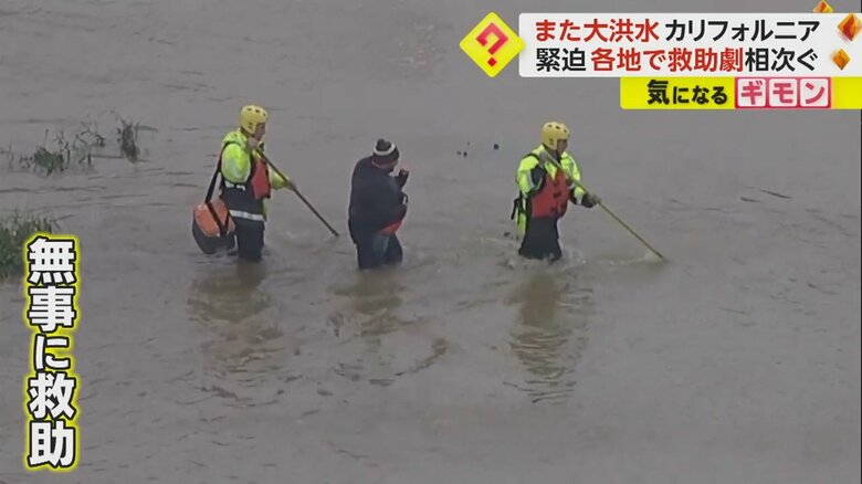 無事に救助され、レスキュー隊と濁流の中を歩く男性