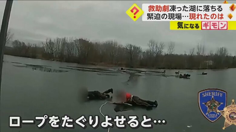 岸からロープでたぐり寄せられた男性と警察官