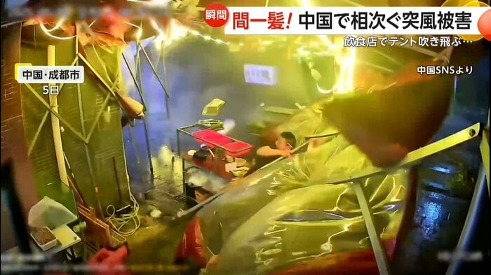 突風で飛ばされるテントを必死に支える男性