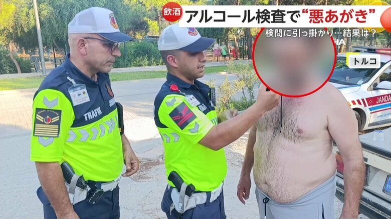 警察官からアルコール検査の器具を差し出され息を吹き込む男性