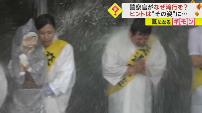 白装束を着て、交通安全のたすきをかけながら滝に打たれる警察官