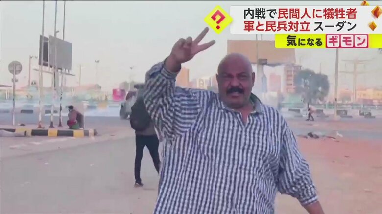 勝利のVマークを掲げる市民のすぐ後ろで催涙弾が撃たれる