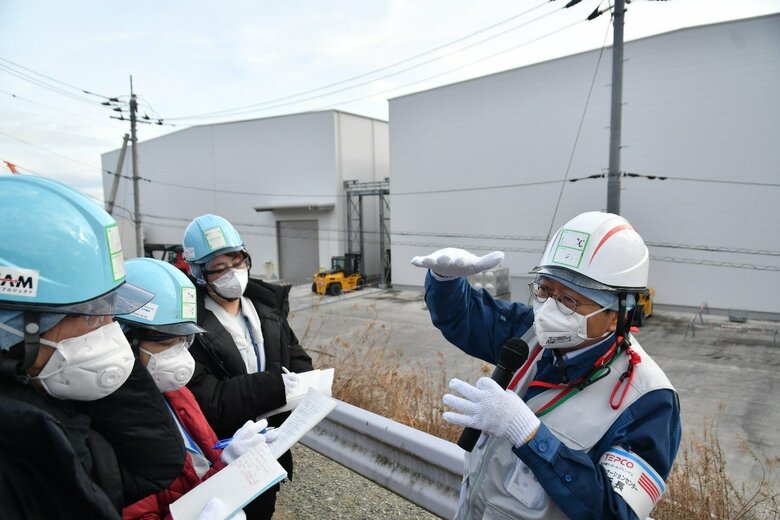 固体廃棄物貯蔵庫前で説明する木元さん　 現在、がれきなどを一時保管するための第11棟を建設中だ（代表撮影）