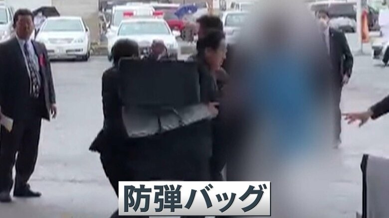 爆発物が投げ入れられた直後、警護が首相を守るように防弾バッグを広げている