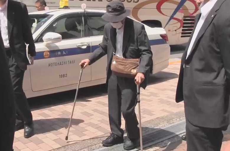 両手に杖をついて歩く飯塚元院長