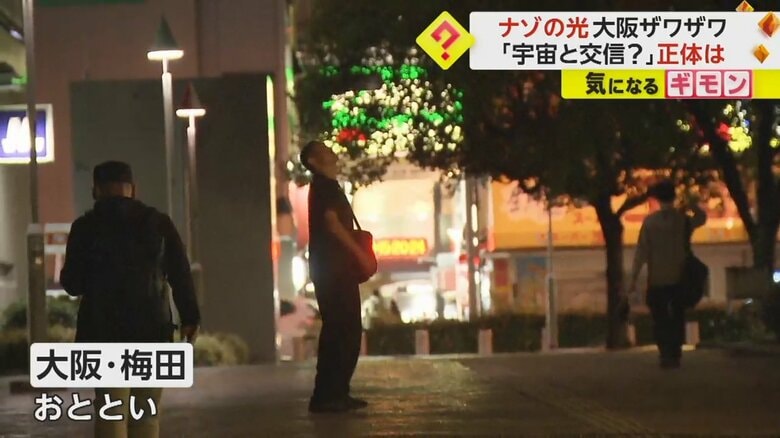 6日、大阪府梅田で「ナゾの光」を見上げる人