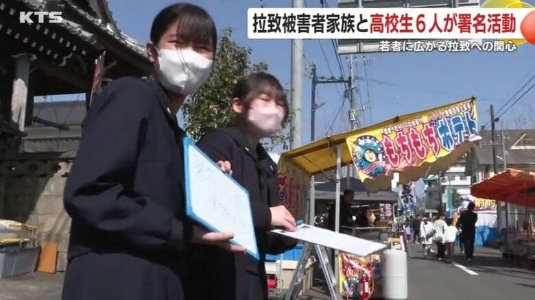 手には「署名活動実施中です」と書いたホワイトボード