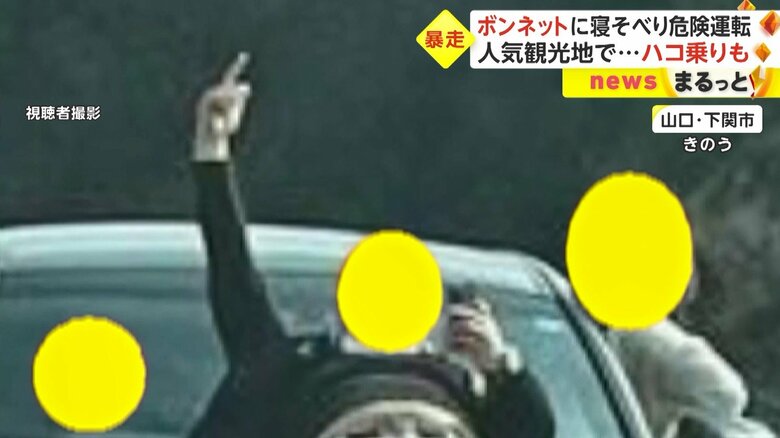 車のボンネットに寝そべり、右手を高く突き上げる男性