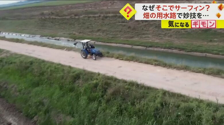 一直線に伸びた用水路の水面を、トラクターに引っ張られて進む男性