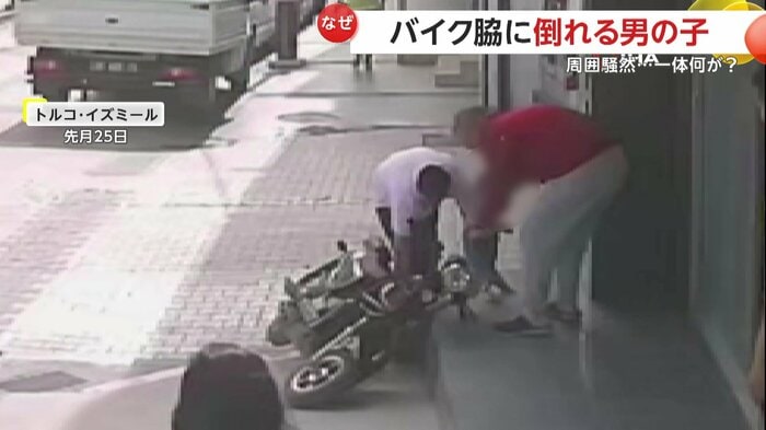 倒れたバイクの横で少年を抱きかかえる父親