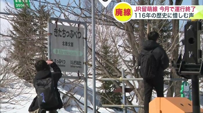 掲示板や駅名の看板などを撮影し別れを惜しむ鉄道ファンたち